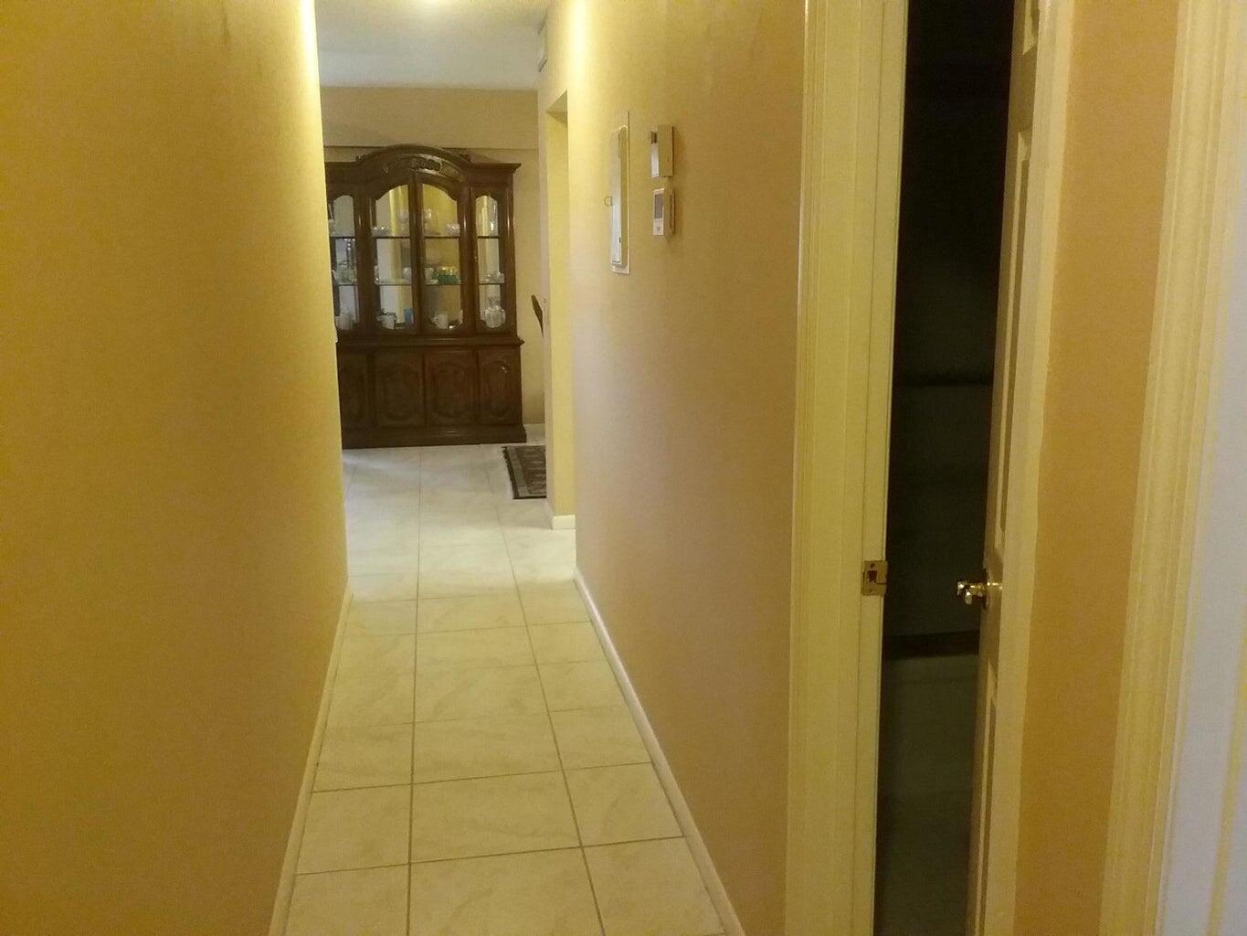 A hallway with beige walls and light-colored tile flooring leads toward a dark wood hutch — 203 Suffolk, Boca Raton FL 33434, BOCA RATON, FL