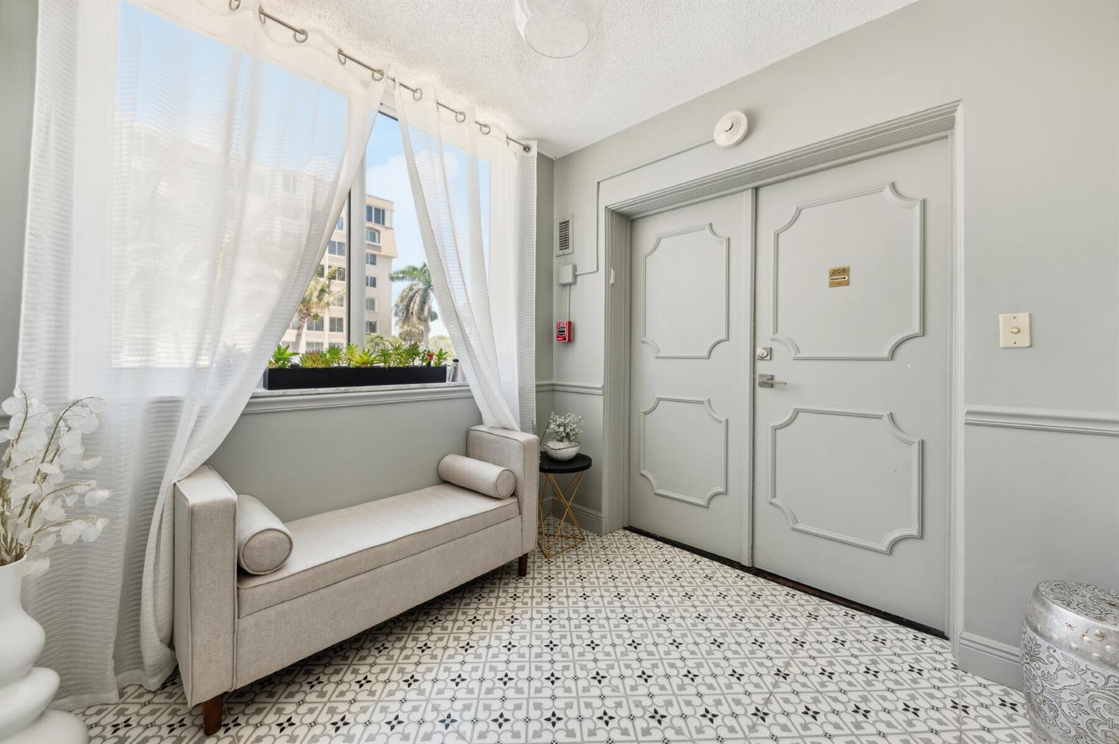 A light-filled entryway features patterned tile flooring, a beige bench, and double doors — 2000 S Ocean Boulevard # 208, Delray Beach FL 33483, DELRAY BEACH, FL