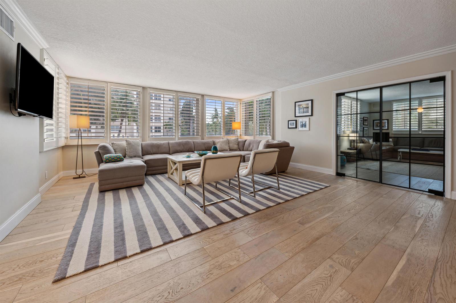A living room features a large sectional sofa, striped rug, and glass-paned room divider — 2000 S Ocean Boulevard # 208, Delray Beach FL 33483, DELRAY BEACH, FL