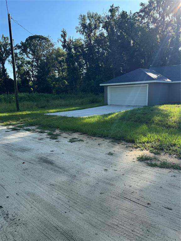 A concrete driveway leads to the garage of a house next to a wooded area — 15045 SE 61 COURT, SUMMERFIELD, FL