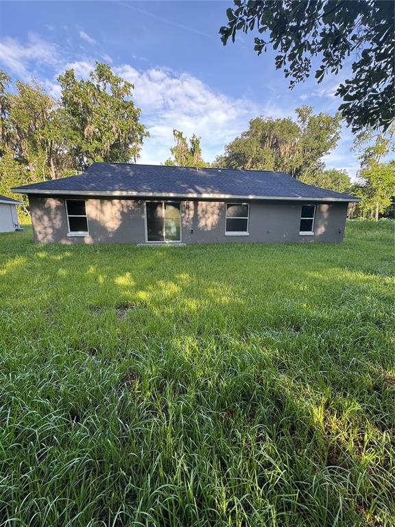 The exterior rear view of a single-story house with a gray facade and sliding glass doors — 15045 SE 61 COURT, SUMMERFIELD, FL