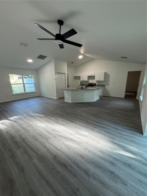 An open-concept living area features light gray wood-look flooring, a kitchen island, and vaulted ceilings — 15045 SE 61 COURT, SUMMERFIELD, FL
