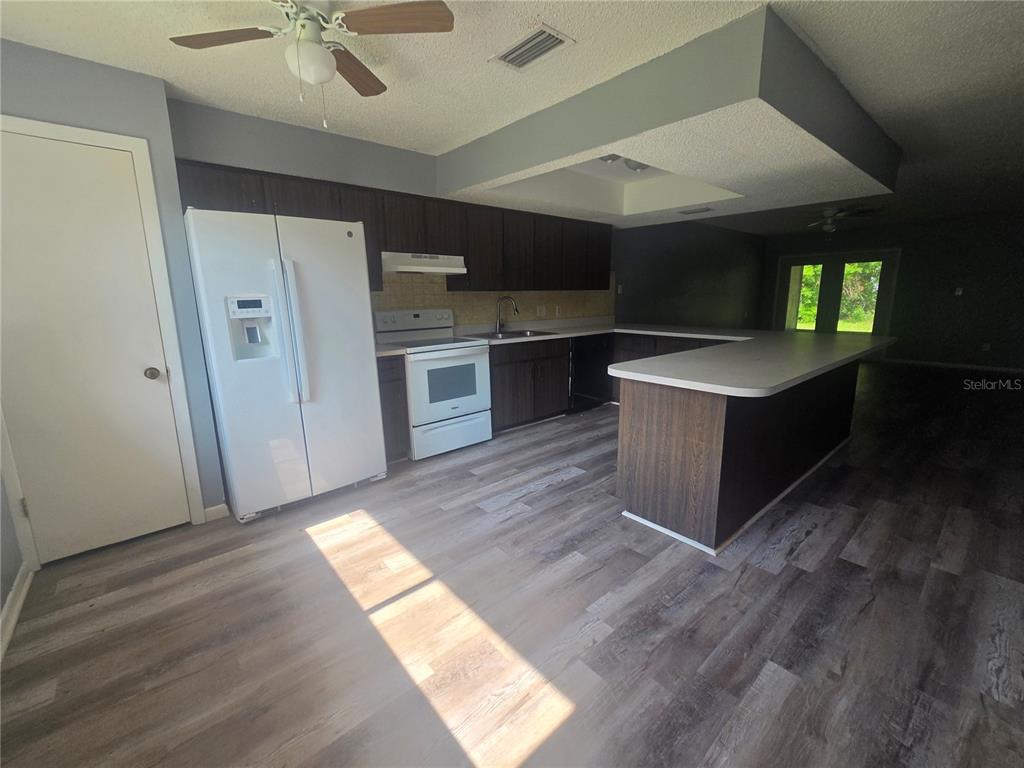 A kitchen features dark wood cabinets, white appliances, a peninsula, and light wood-look flooring — 1316 MARKHAM AVENUE UNIT B, SPRING HILL, FL