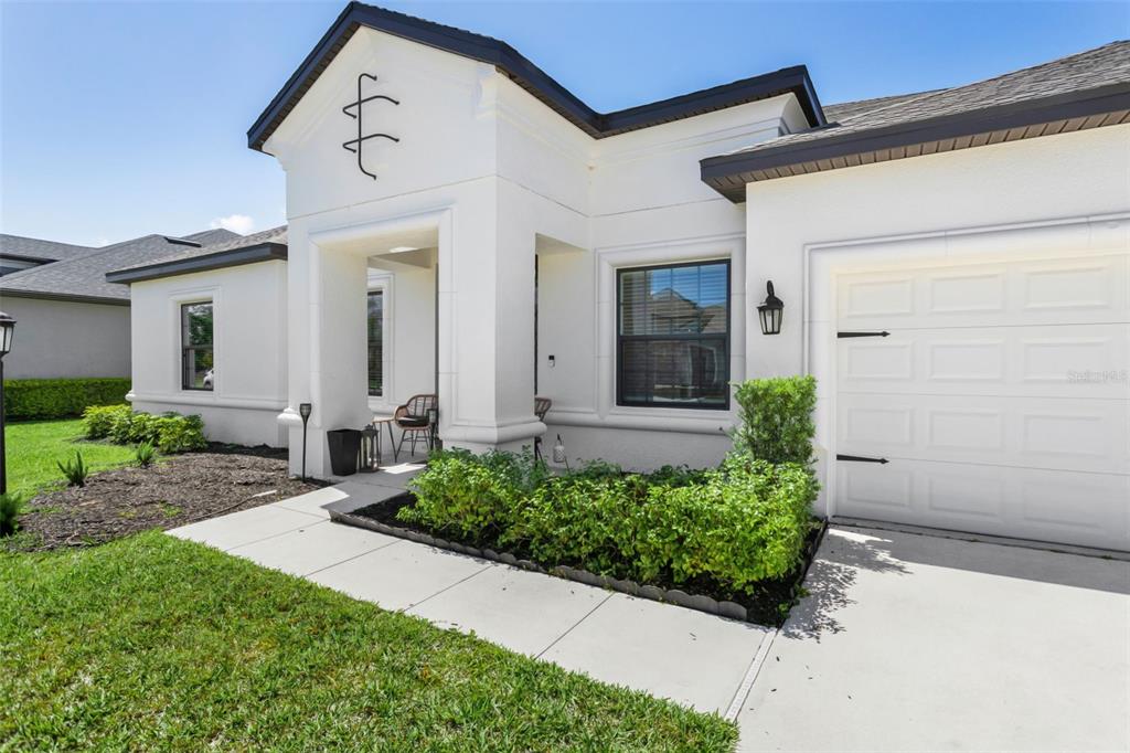 The exterior of a white stucco house features a covered entryway, garage, and landscaped lawn — 4520 POND BROOK COURT, LAKEWOOD RANCH, FL