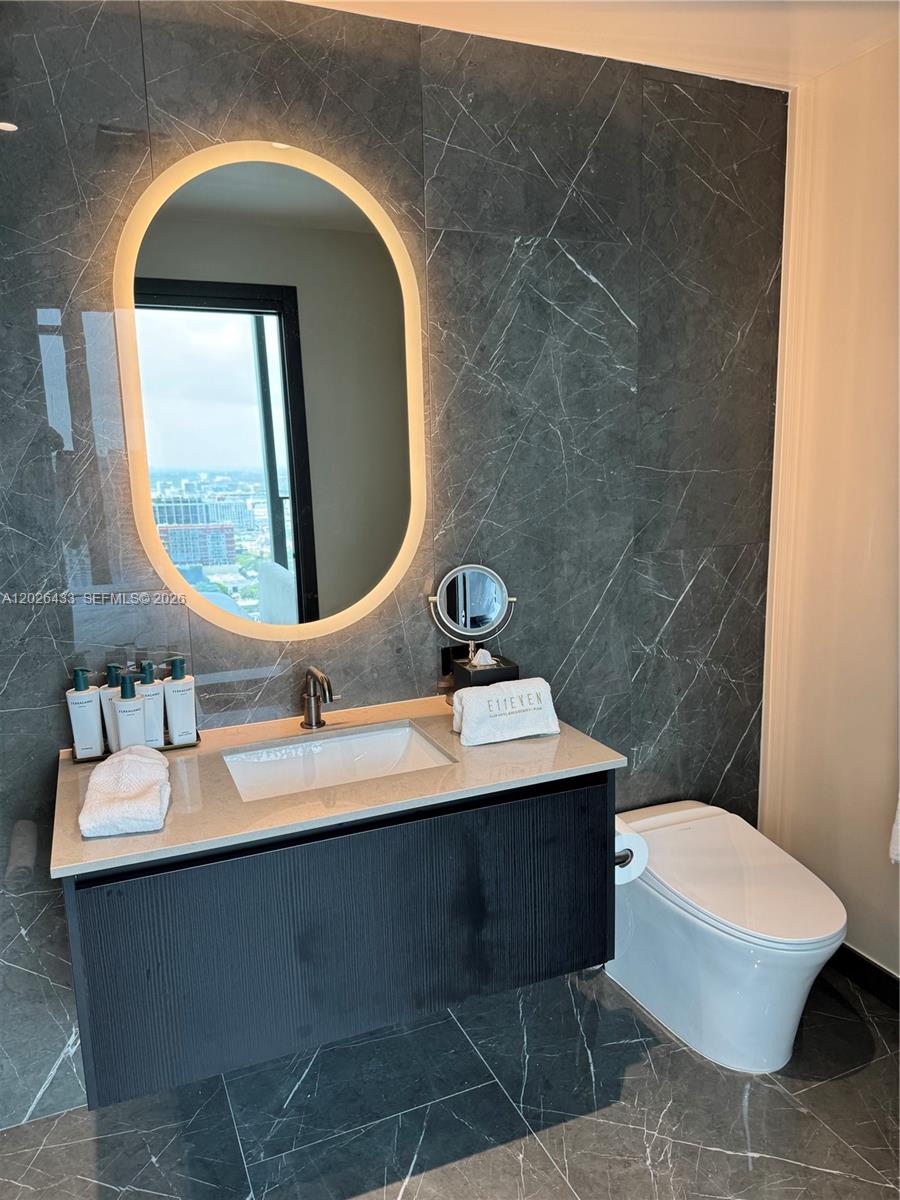 A modern bathroom features dark marble walls, a floating vanity, and an illuminated oval mirror — 20 NE 11th St # 3405, Miami FL 33132, MIAMI, FL
