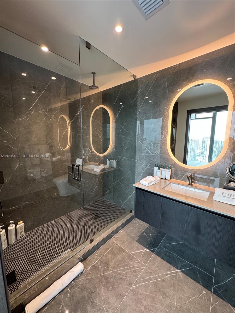 A modern bathroom features dark marble walls, a glass-enclosed shower, and a floating vanity — 20 NE 11th St # 3405, Miami FL 33132, MIAMI, FL
