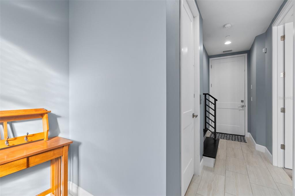 A hallway with light blue walls, tile flooring, a wooden console table, and a white door — 129 S PARK AVENUE UNIT 8E, WINTER GARDEN, FL