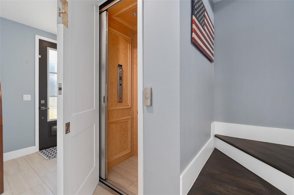 A residential elevator with wood paneling is situated next to a staircase and entryway — 129 S PARK AVENUE UNIT 8E, WINTER GARDEN, FL