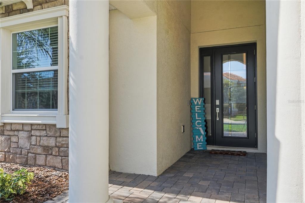 A covered entryway features a stone-accented wall, a white pillar, and a dark front door — 8954 FLUFFY LIE COURT, DAVENPORT, FL