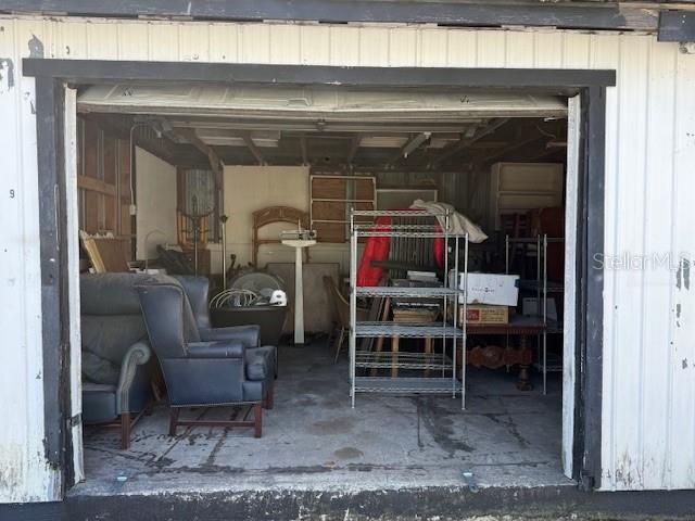 A cluttered garage contains a dark armchair, metal shelving units, and various pieces of furniture — 323 N DELAWARE AVENUE UNIT 9, DELAND, FL