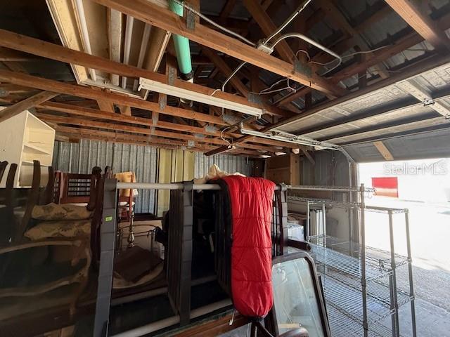 An interior view of a cluttered garage with exposed wooden rafters and metal shelving — 323 N DELAWARE AVENUE UNIT 9, DELAND, FL