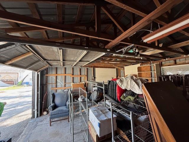 A cluttered garage with exposed wooden rafters, a metal door, and various storage items — 323 N DELAWARE AVENUE UNIT 9, DELAND, FL