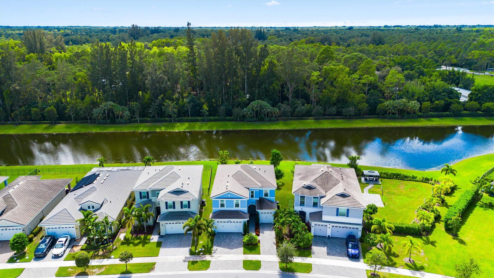 An aerial view shows four suburban houses with tiled roofs situated along a canal — 15662 Orchard Drive, Westlake FL 33470, WESTLAKE, FL