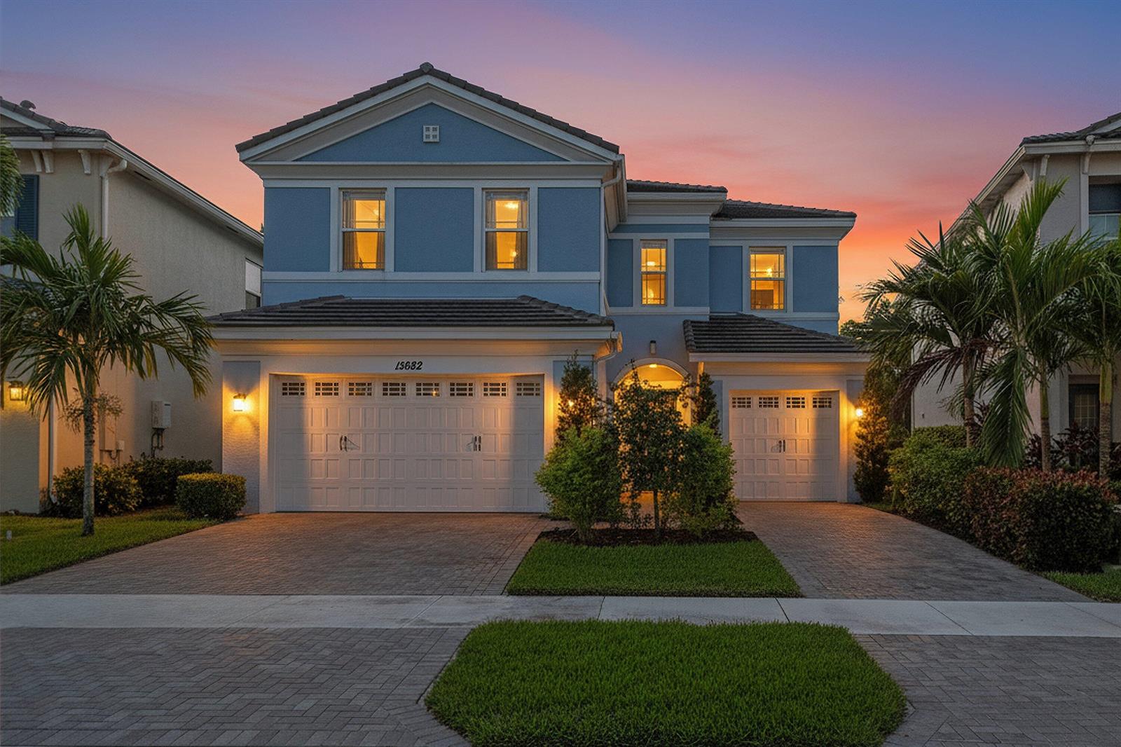 A two-story blue house with a three-car garage and a paved driveway at sunset — 15662 Orchard Drive, Westlake FL 33470, WESTLAKE, FL