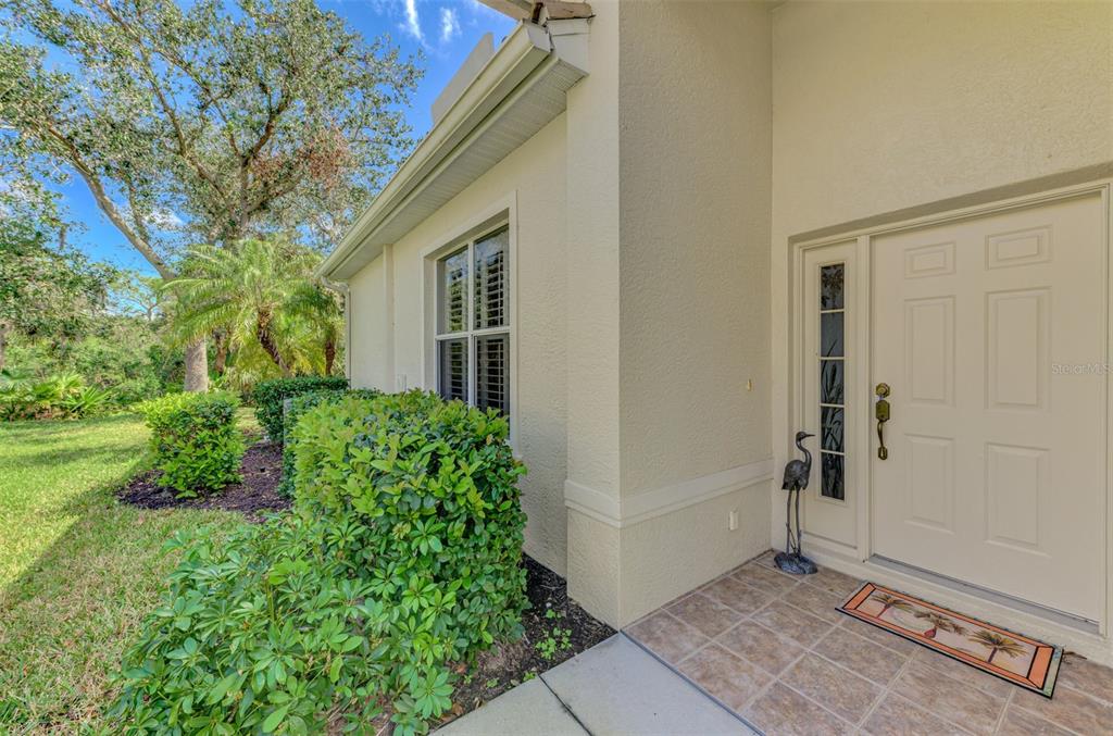 A beige house exterior features a front door with a sidelight, tiled porch, and landscaping — 14298 RESERVE COURT, PORT CHARLOTTE, FL