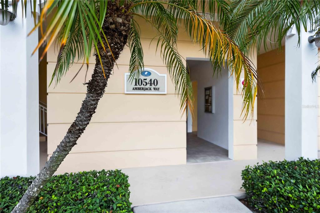 A palm tree stands in front of a building entrance with a numbered address sign — 10540 AMBERJACK WAY UNIT 102, ENGLEWOOD, FL