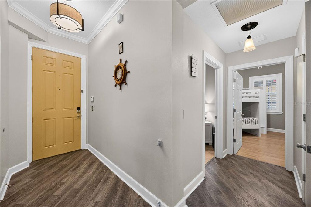 An entryway with a yellow door, wood-look flooring, and a view into a bedroom — 10540 AMBERJACK WAY UNIT 102, ENGLEWOOD, FL