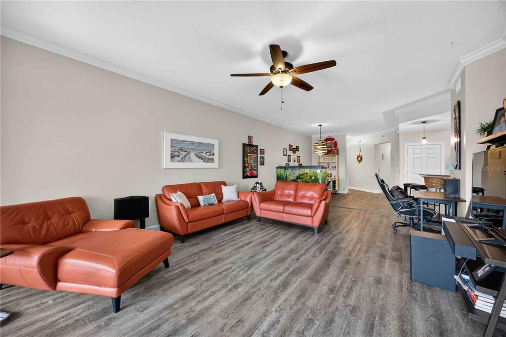 A living room features orange leather sofas, wood-look flooring, and a ceiling fan — 10540 AMBERJACK WAY UNIT 102, ENGLEWOOD, FL