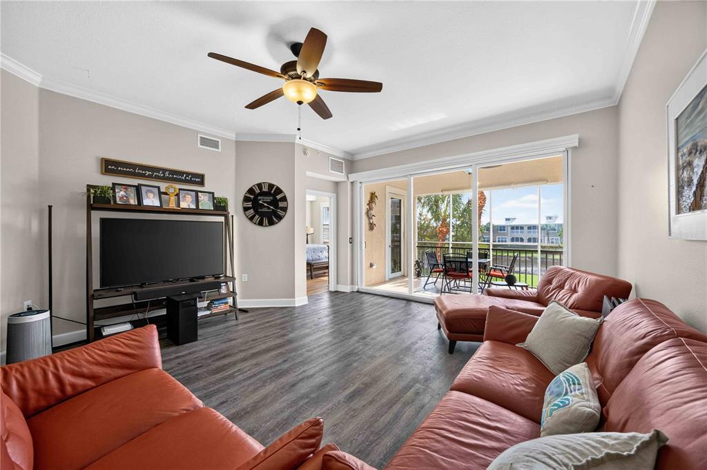 A living room features a large television, leather sofas, a ceiling fan, and a sliding door — 10540 AMBERJACK WAY UNIT 102, ENGLEWOOD, FL