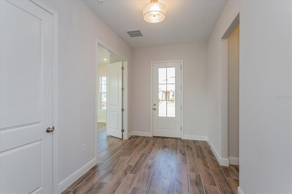 A bright entryway features wood-look tile flooring, white walls, and a glass-paneled front door — 10078 DULBECCO STREET, ORLANDO, FL