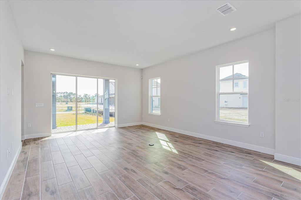An empty room with wood-look tile flooring, white walls, large windows, and a sliding glass door — 10078 DULBECCO STREET, ORLANDO, FL