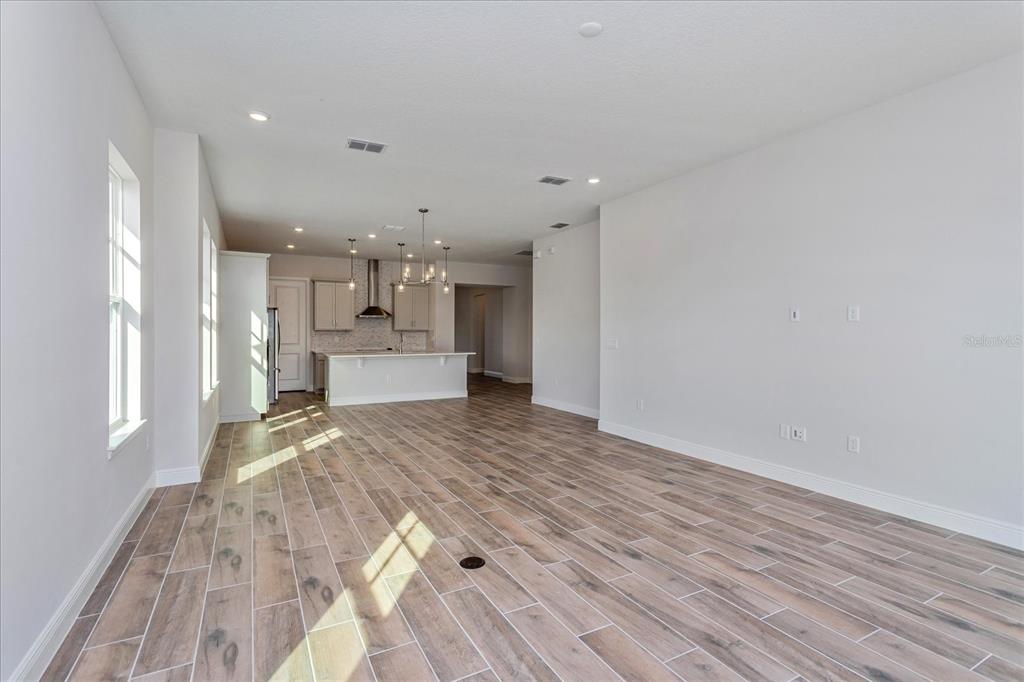An open-concept living area features wood-look tile flooring, white walls, and a kitchen with an island — 10078 DULBECCO STREET, ORLANDO, FL
