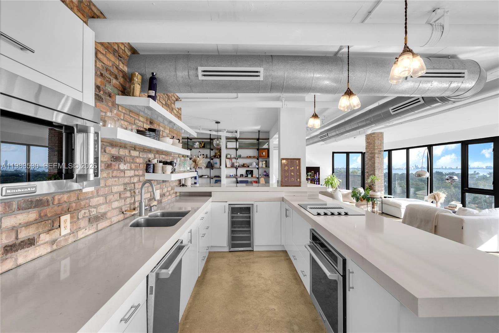A modern kitchen features white cabinetry, quartz countertops, exposed brick walls, and industrial ductwork — 5701 Biscayne Blvd # 9, Miami FL 33137, MIAMI, FL