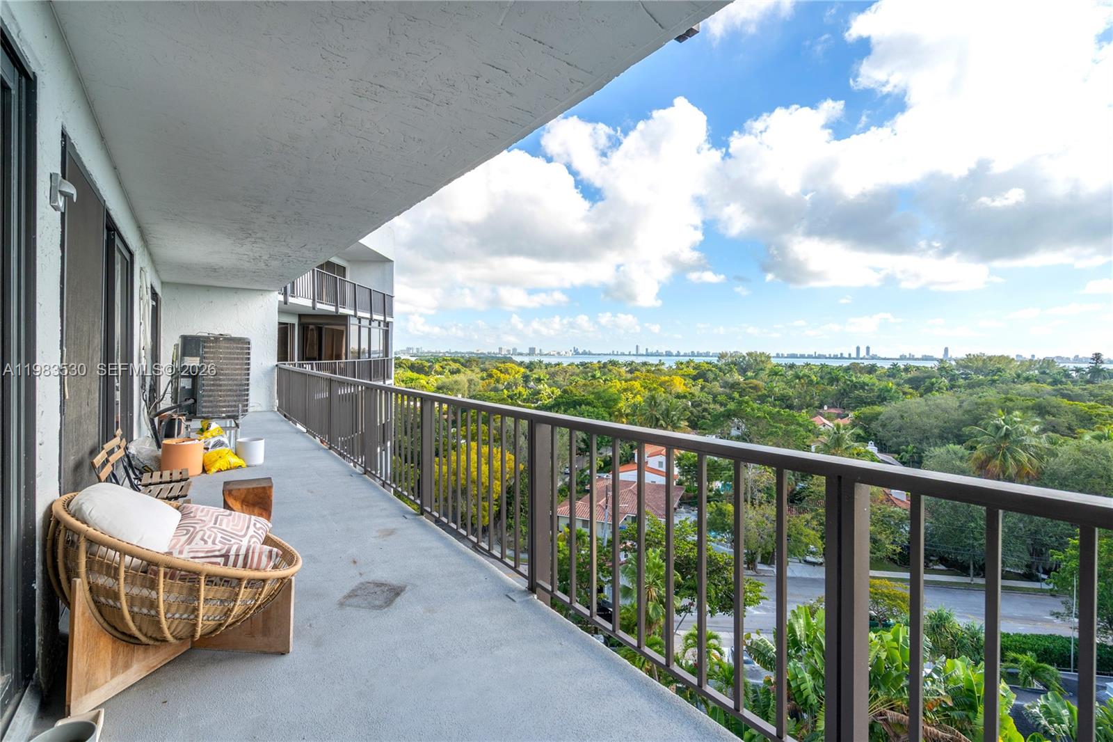 A balcony with a wicker chair overlooks a lush green landscape and distant city skyline — 5701 Biscayne Blvd # 9, Miami FL 33137, MIAMI, FL