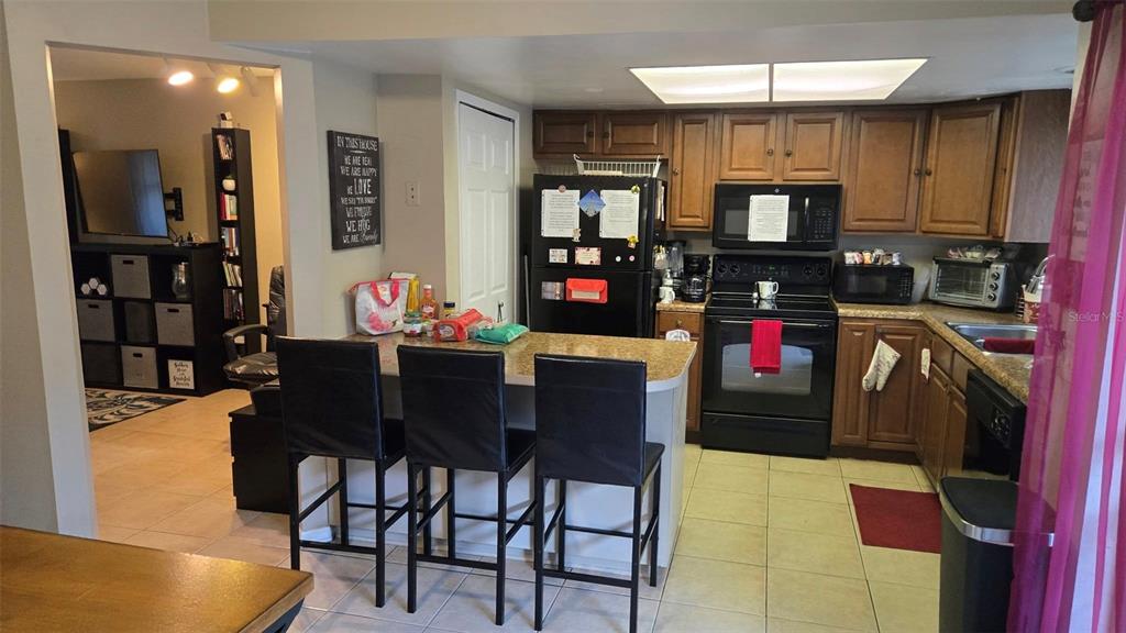 A kitchen with wooden cabinets, black appliances, and a breakfast bar with three black chairs — 5433 BROOKSWOOD WAY UNIT 806, ORLANDO, FL