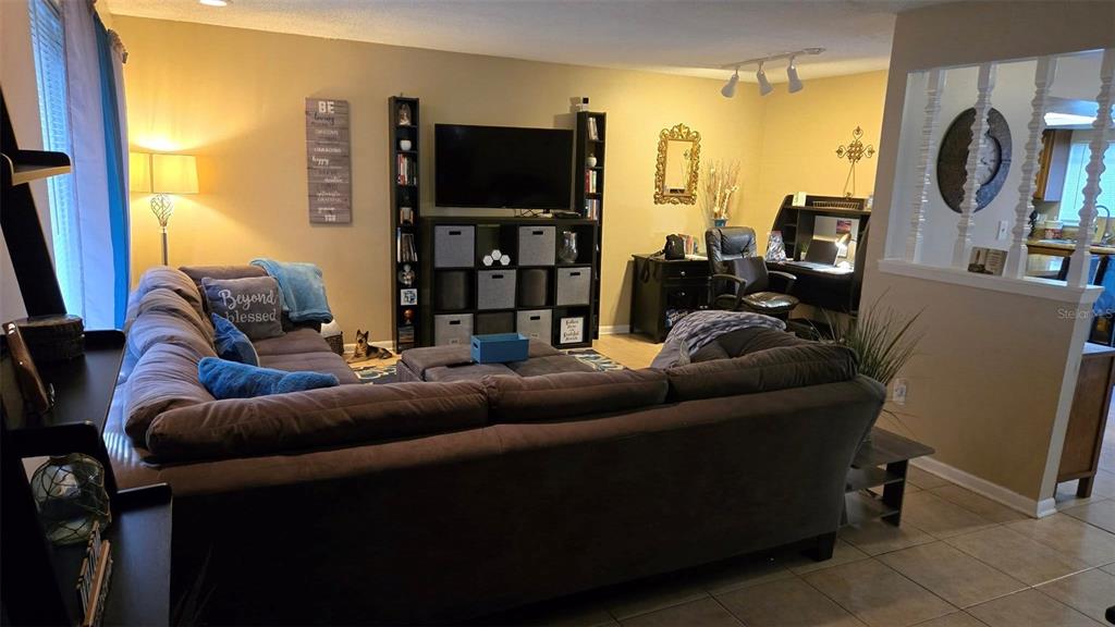 A living room features a large sectional sofa, a television on a shelving unit, and a desk — 5433 BROOKSWOOD WAY UNIT 806, ORLANDO, FL
