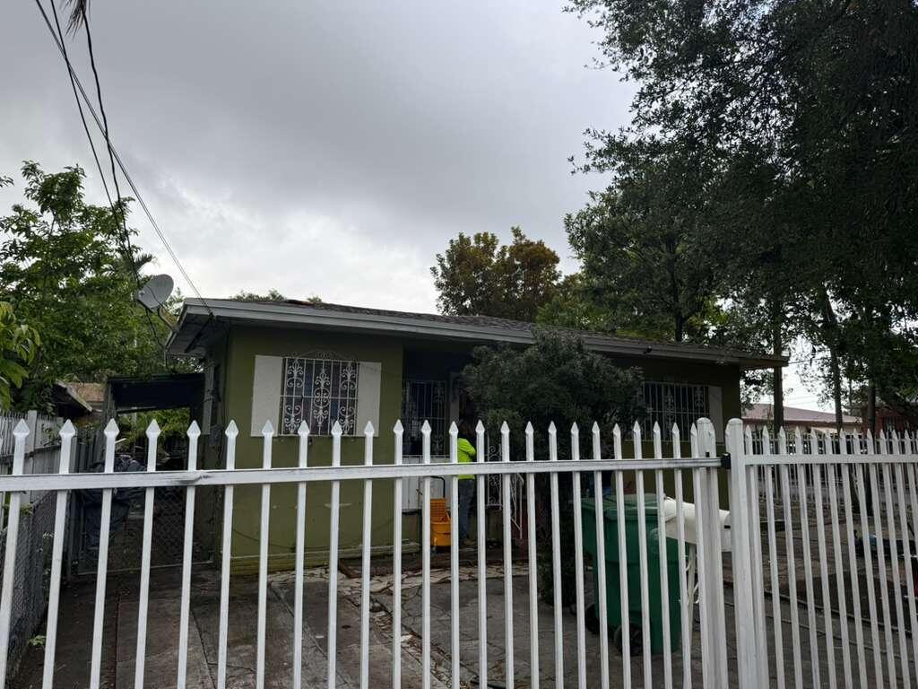 A green single-story house is viewed from behind a white metal picket fence — 139 NE 63rd Street, Miami FL 33138, MIAMI, FL