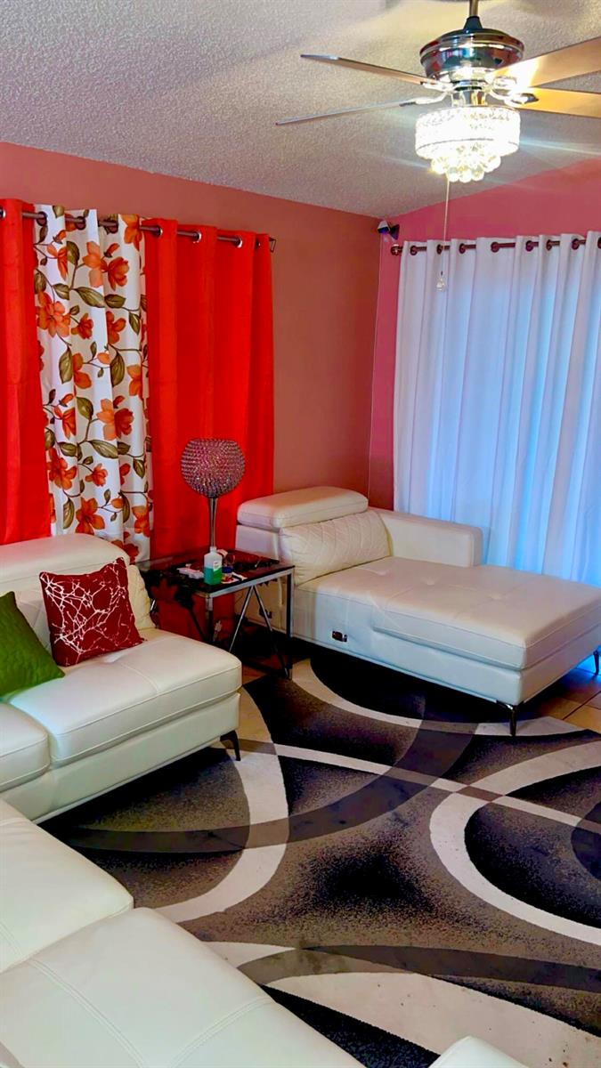 A living room features white leather furniture, a patterned area rug, and bright orange curtains — 2004 Maplewood Drive # 2004, FL 33415, FL