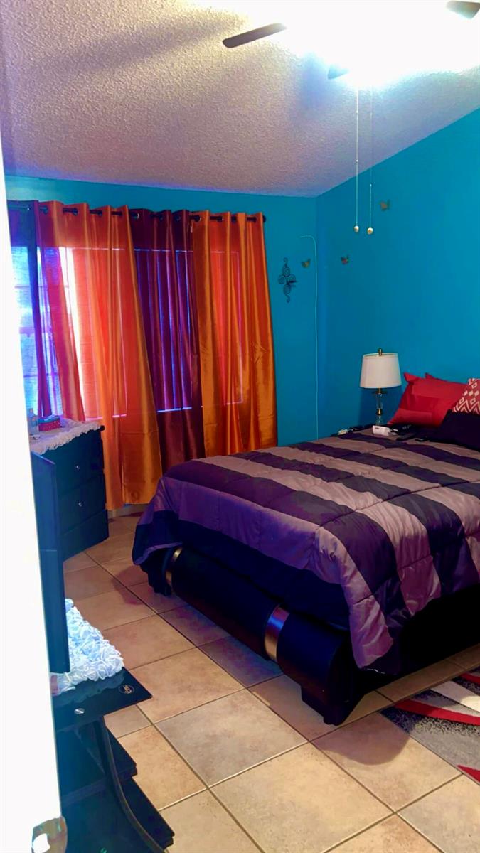 A bedroom features bright blue walls, a dark bed frame, and vibrant orange and red curtains — 2004 Maplewood Drive # 2004, FL 33415, FL
