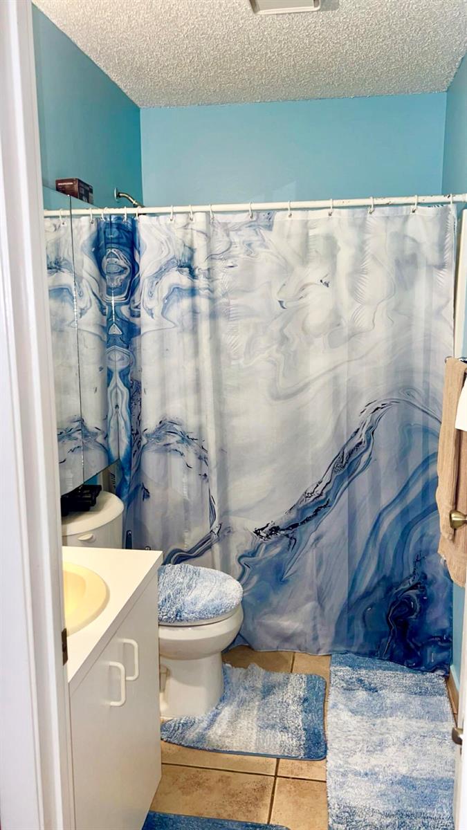 A bathroom features a blue marble-patterned shower curtain, matching toilet lid cover, and blue rugs — 2004 Maplewood Drive # 2004, FL 33415, FL