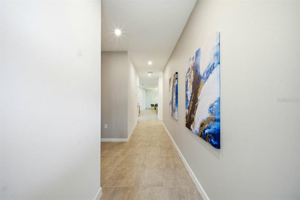 A hallway with tile flooring features two abstract paintings on the right wall — 2328 SALTY WINDS WAY, KISSIMMEE, FL