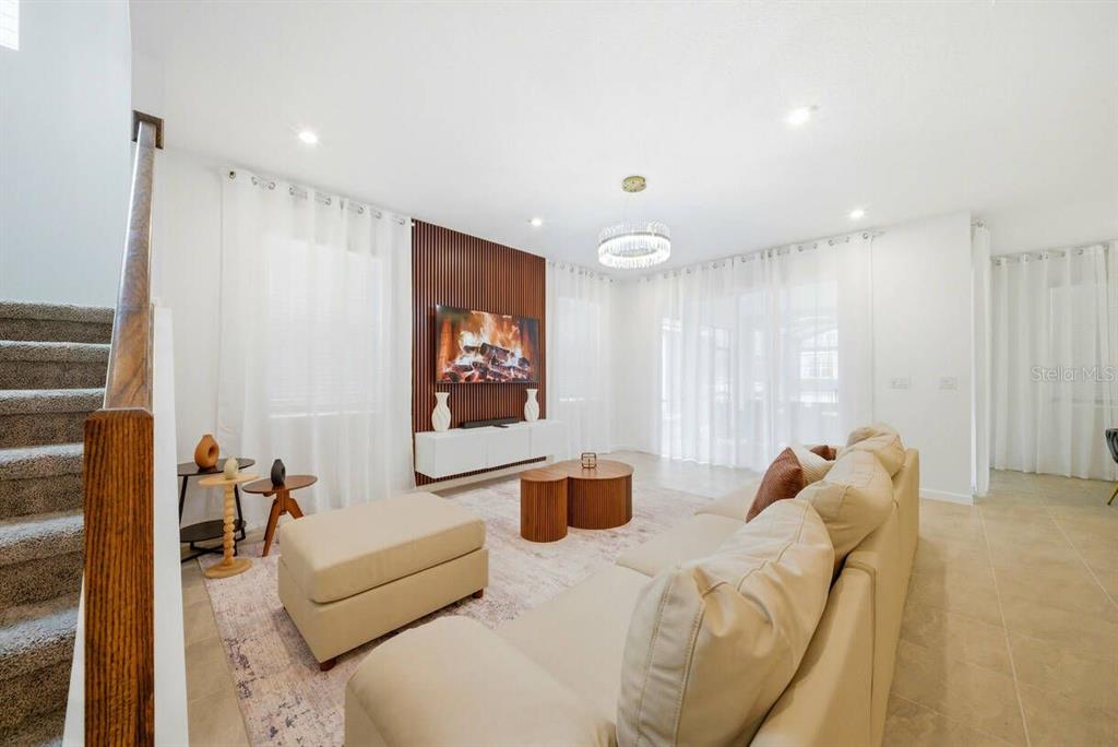 A living room features a wood-slat accent wall with a television, beige sofa, and stairs — 2328 SALTY WINDS WAY, KISSIMMEE, FL