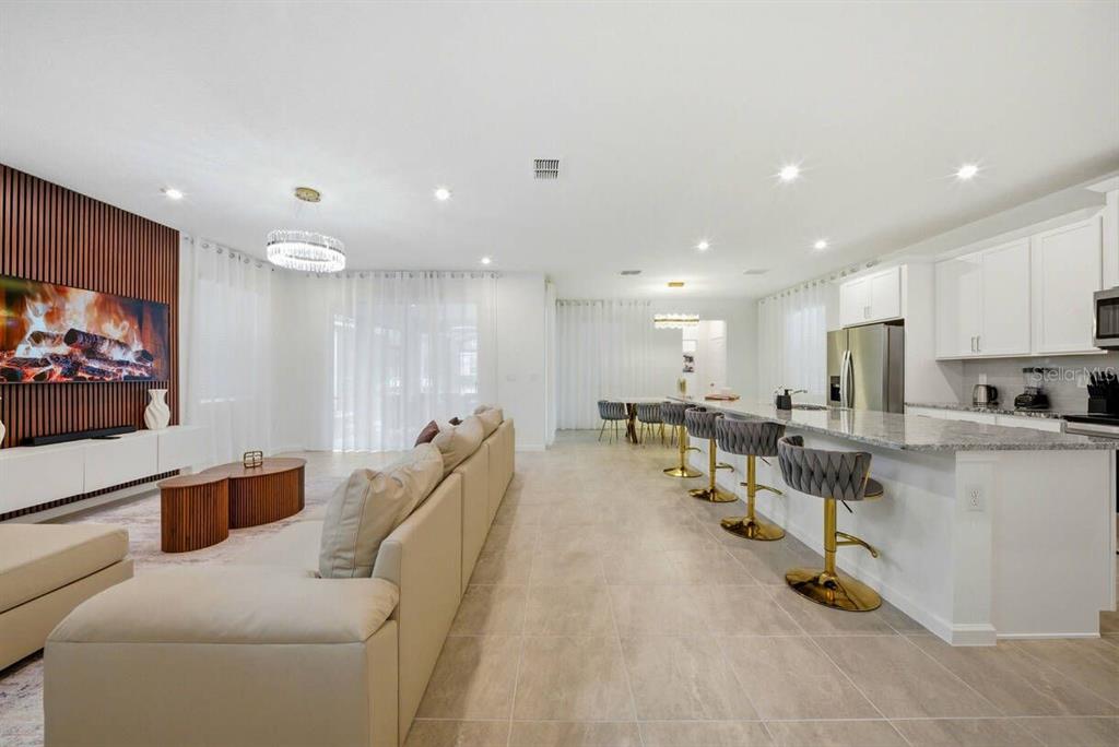 An open-concept living room and kitchen featuring white cabinetry, a large island, and wood accents — 2328 SALTY WINDS WAY, KISSIMMEE, FL