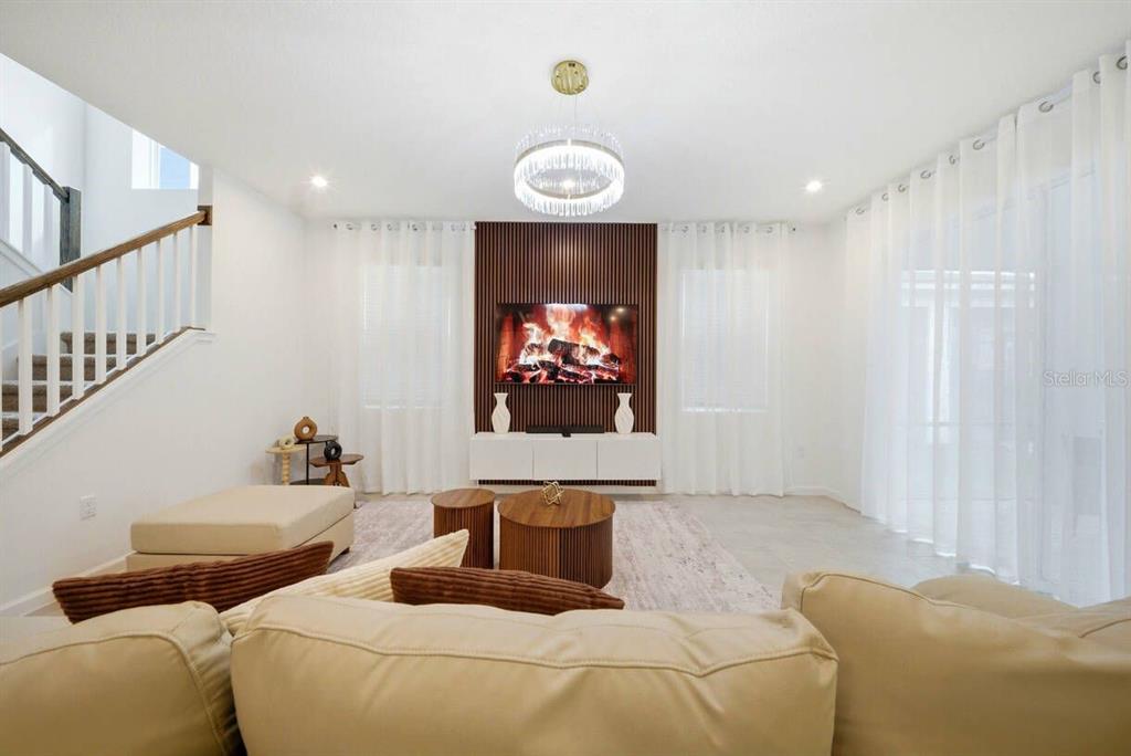 A living room features a wood-slat accent wall with a television, white cabinetry, and stairs — 2328 SALTY WINDS WAY, KISSIMMEE, FL