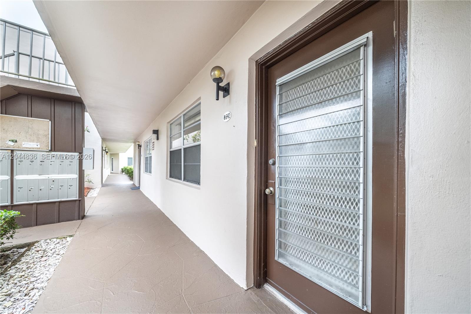 An exterior walkway features a brown door with a security screen and a wall-mounted light — 642 N Normandy  N # 642, Delray Beach FL 33484, DELRAY BEACH, FL