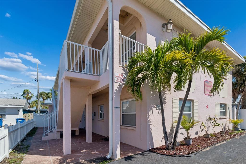 A two-story pink stucco building features an exterior staircase and a palm tree out front — 525 73RD AVE UNIT 5, ST PETE BEACH, FL