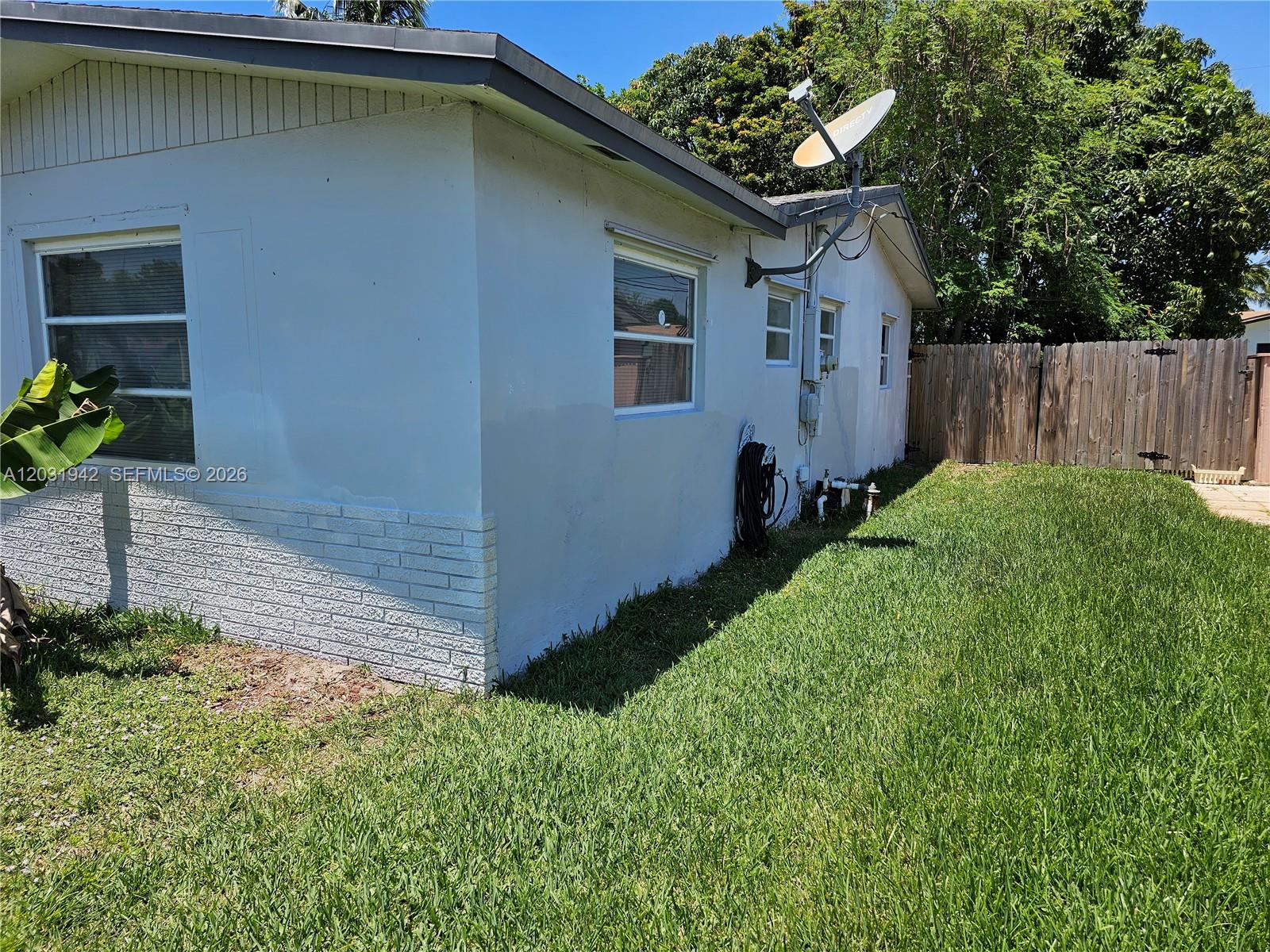 The exterior side of a light-colored house features a brick base and a satellite dish — 4431 NW 23rd Ct, Lauderhill FL 33313, LAUDERHILL, FL