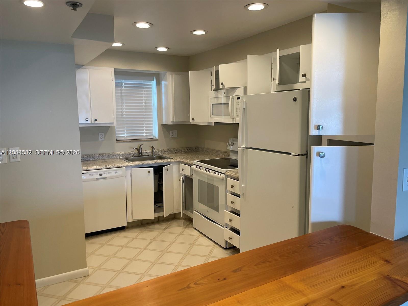 A kitchen features white cabinets, white appliances, and granite countertops with a tiled floor — 3100 W Rolling Hills Cir # 502, Davie FL 33328, DAVIE, FL