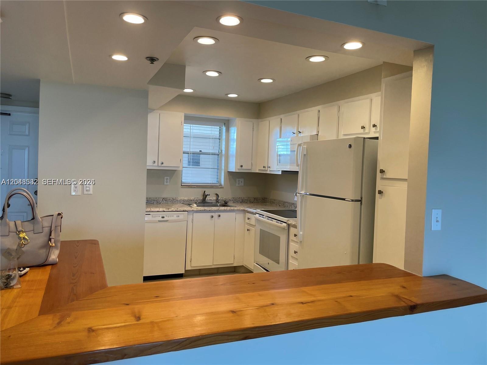 A kitchen features white cabinets, white appliances, granite countertops, and a wooden breakfast bar — 3100 W Rolling Hills Cir # 502, Davie FL 33328, DAVIE, FL