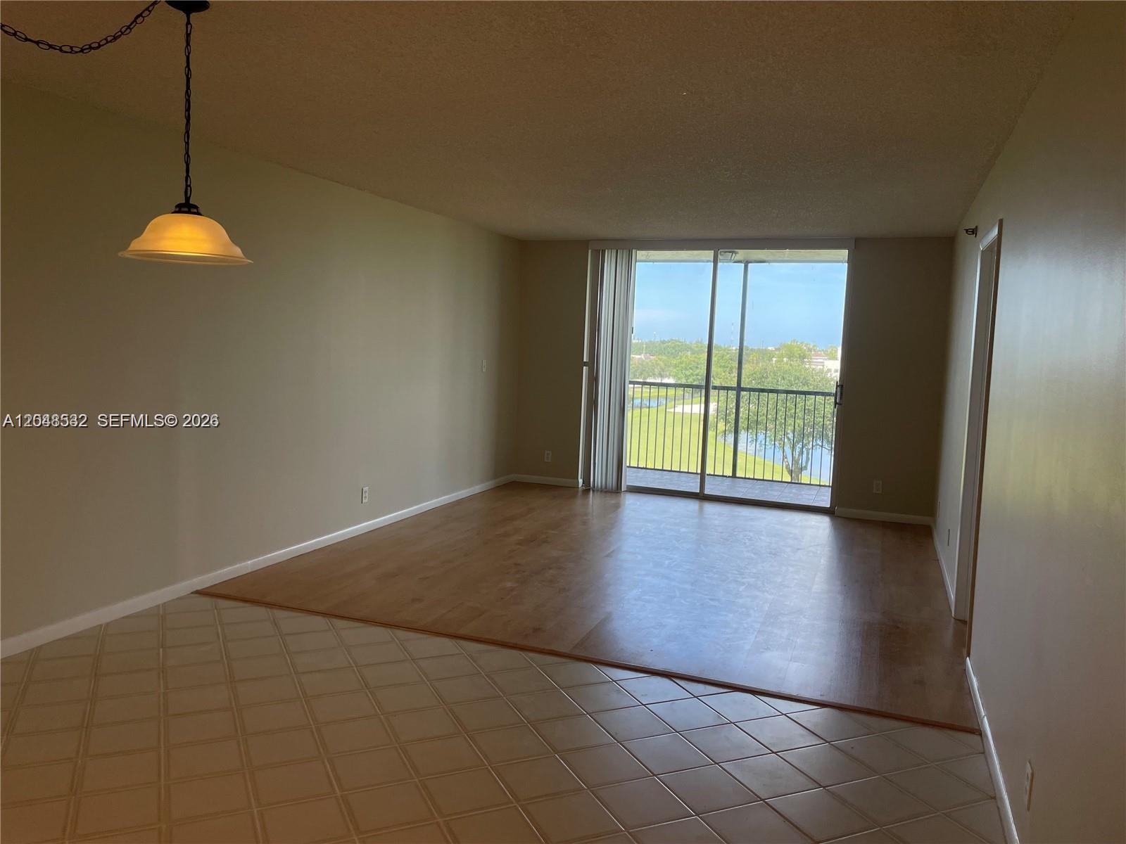 An empty living room features tile and wood flooring, a hanging light, and a balcony — 3100 W Rolling Hills Cir # 502, Davie FL 33328, DAVIE, FL