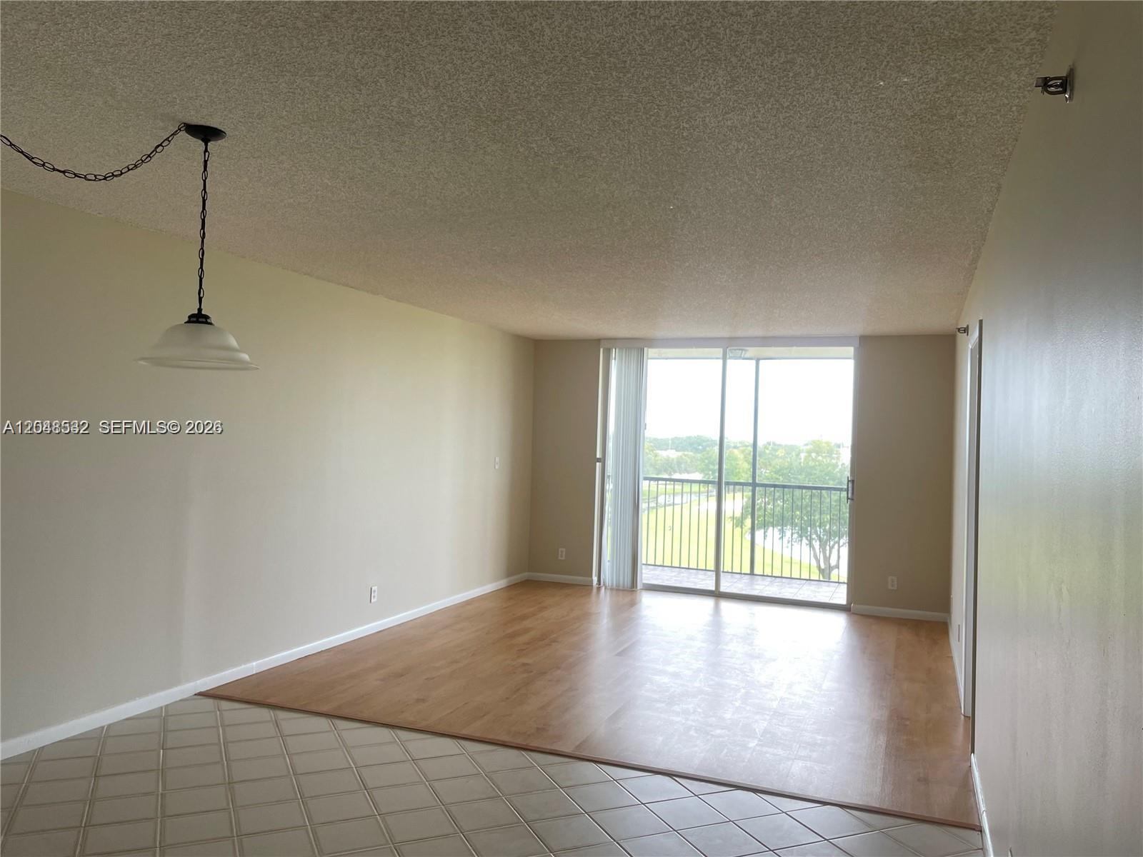 An empty room features light wood flooring, a tile transition area, and a balcony view — 3100 W Rolling Hills Cir # 502, Davie FL 33328, DAVIE, FL