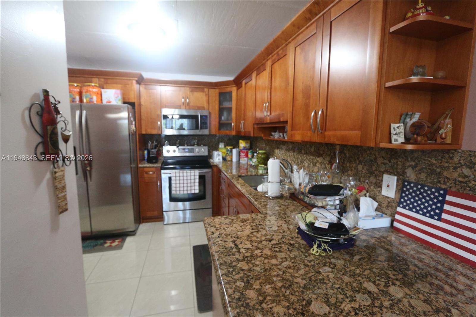 A kitchen features wood cabinets, granite countertops, stainless steel appliances, and tile flooring — 6940 NW Miami Gardens Dr # 430, Hialeah FL 33015, HIALEAH, FL