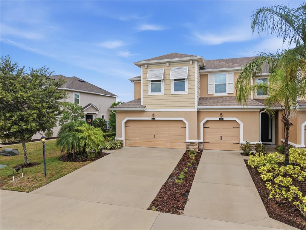 A two-story duplex with tan stucco and siding, two garage doors, and a concrete driveway — 5553 PLEASANTVIEW COURT, BRADENTON, FL