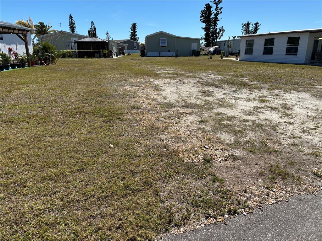A vacant, grassy lot sits between several manufactured homes under a clear blue sky — 7527 SILAGE CIRCLE, PORT CHARLOTTE, FL