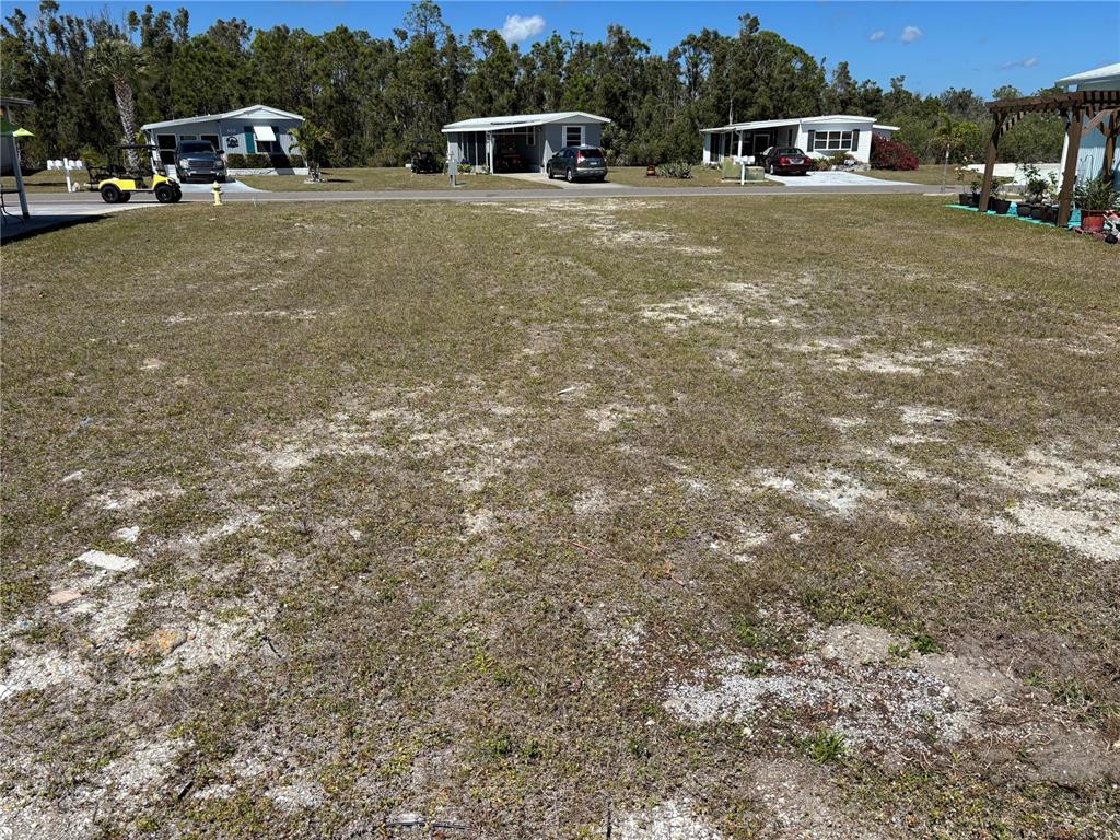 A vacant, grassy residential lot sits in front of several manufactured homes under a blue sky — 7527 SILAGE CIRCLE, PORT CHARLOTTE, FL