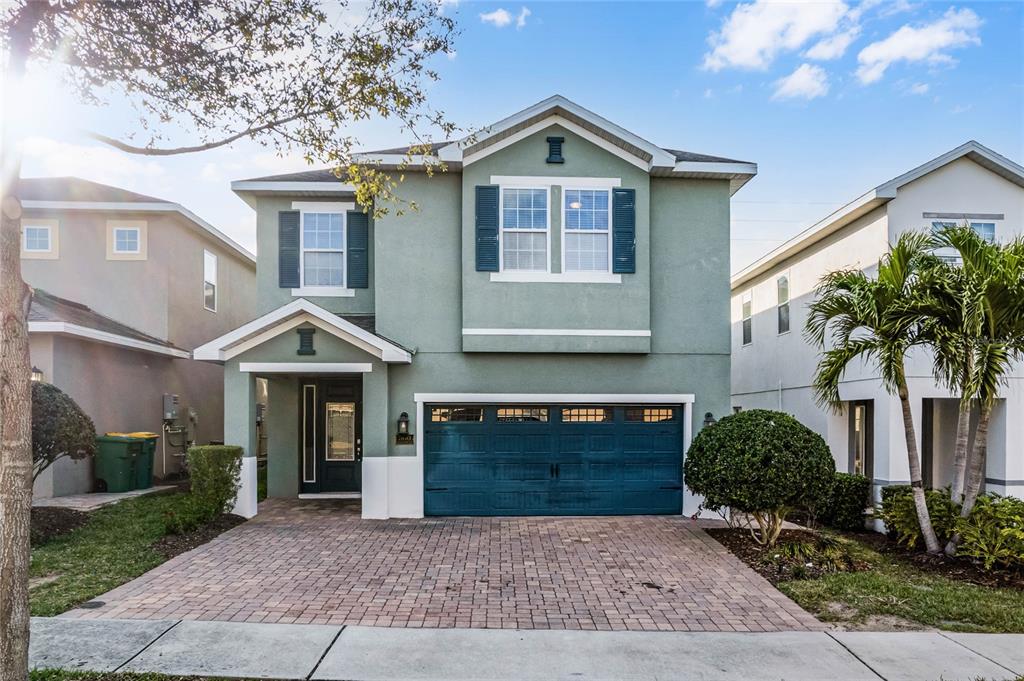 A two-story green house with a brick driveway, a two-car garage, and dark shutters — 350 PENDANT COURT, KISSIMMEE, FL